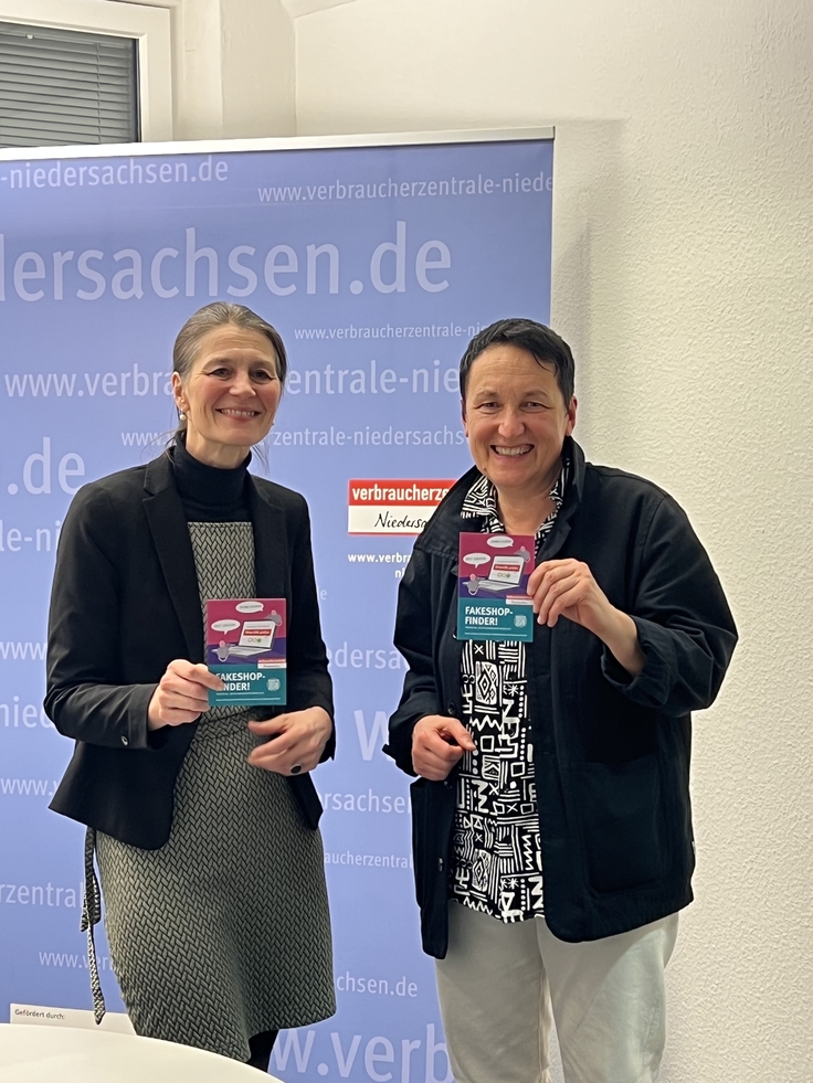 Ministerin Miriam Staudte (links) beim Besuch der Verbraucherzentrale mit Petra Kristandt vor einem Banner der Verbraucherzentrale Niedersachsen stehend